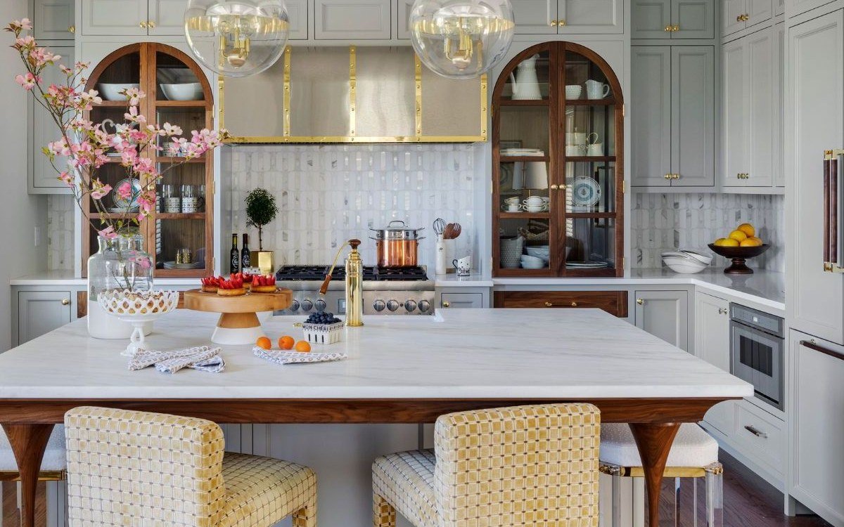 Kitchen with arched glass-front display cabinets, stone island and brass pendant lighting