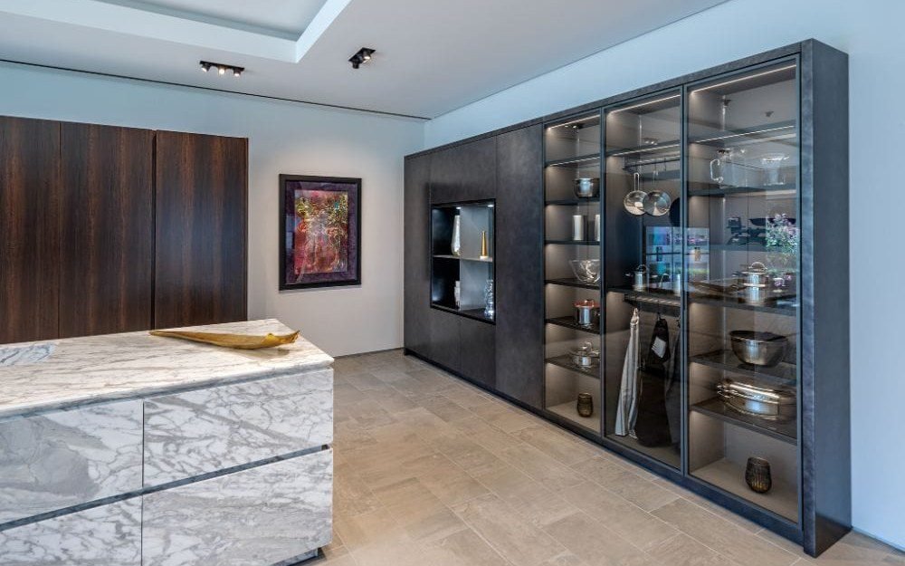 Dark glass-front display cabinets with lit shelving and a marble-top island