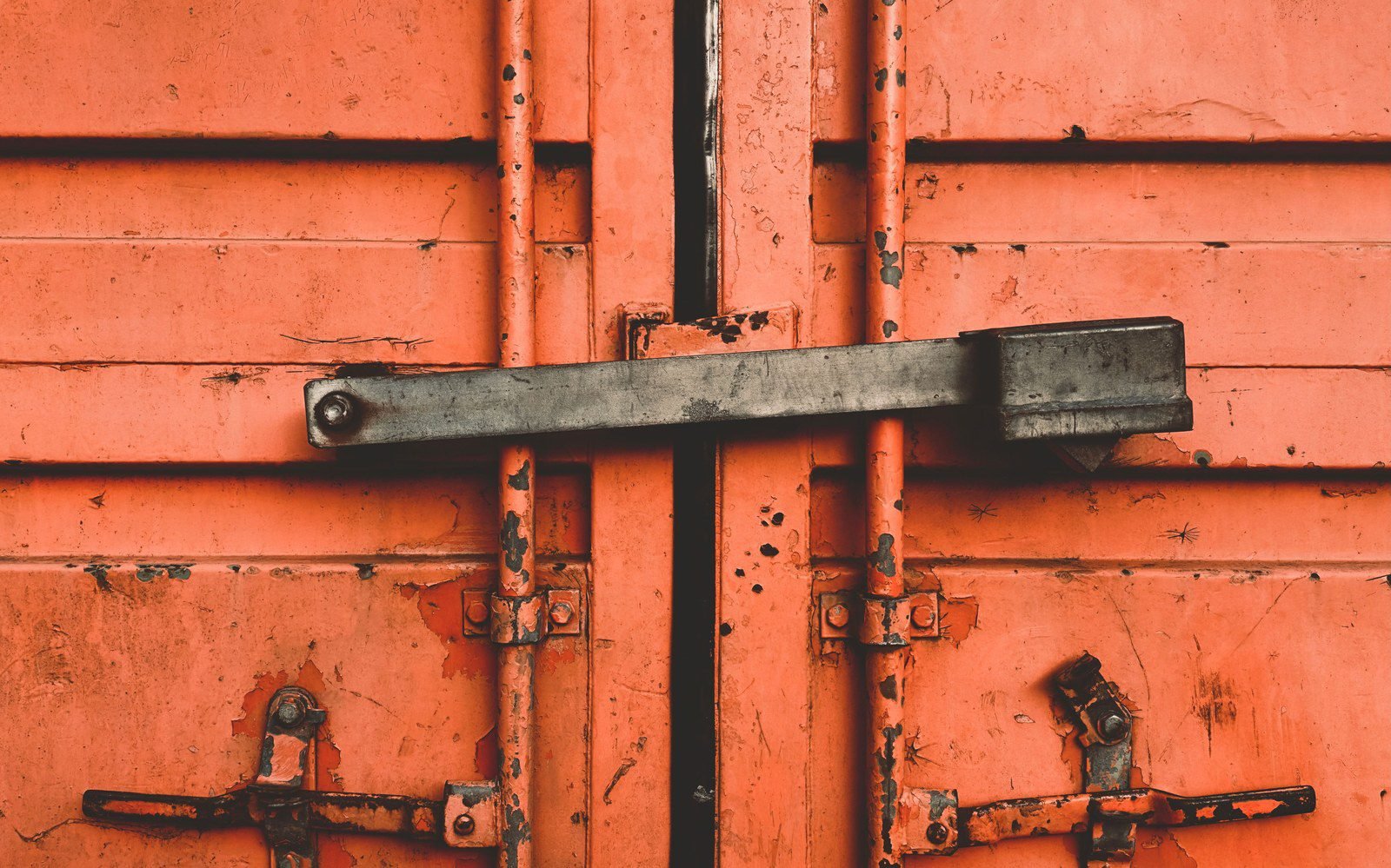 Weathered orange container door with a steel latch at a shipping yard