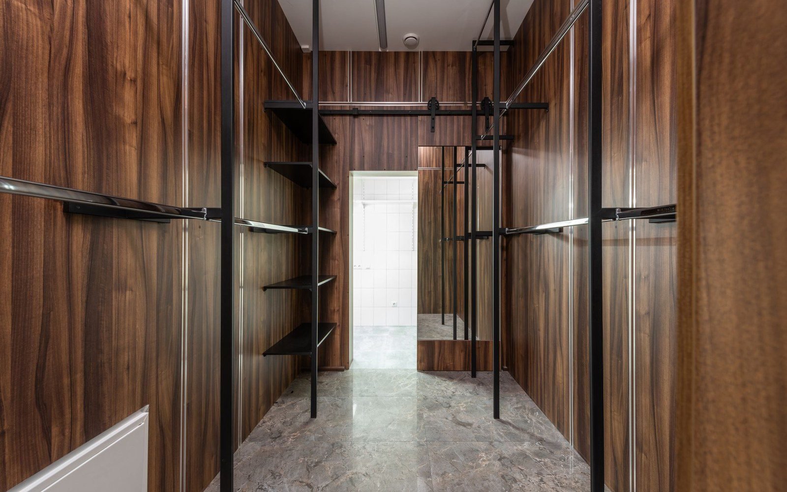 Dark wood walk-in closet with central aisle between two cabinetry walls