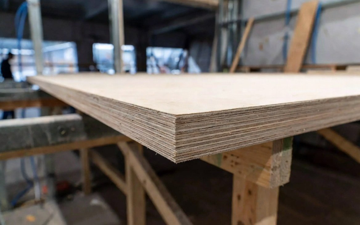 Plywood panel with its layered core on a factory bench — the board stock specified on the BOM