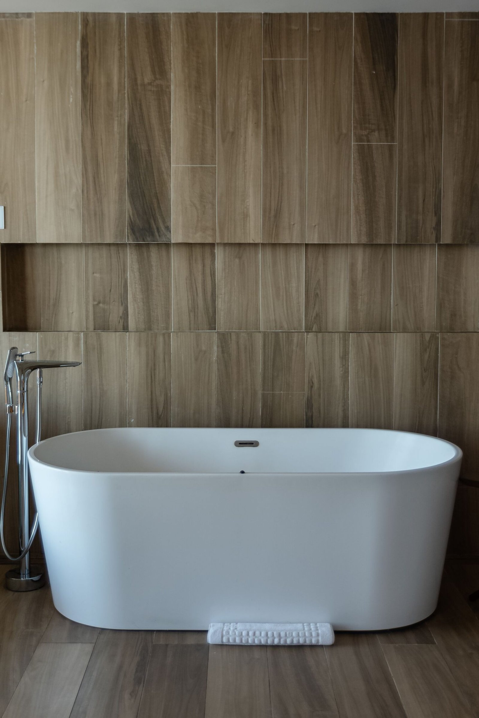 White freestanding tub against a walnut panelled wall
