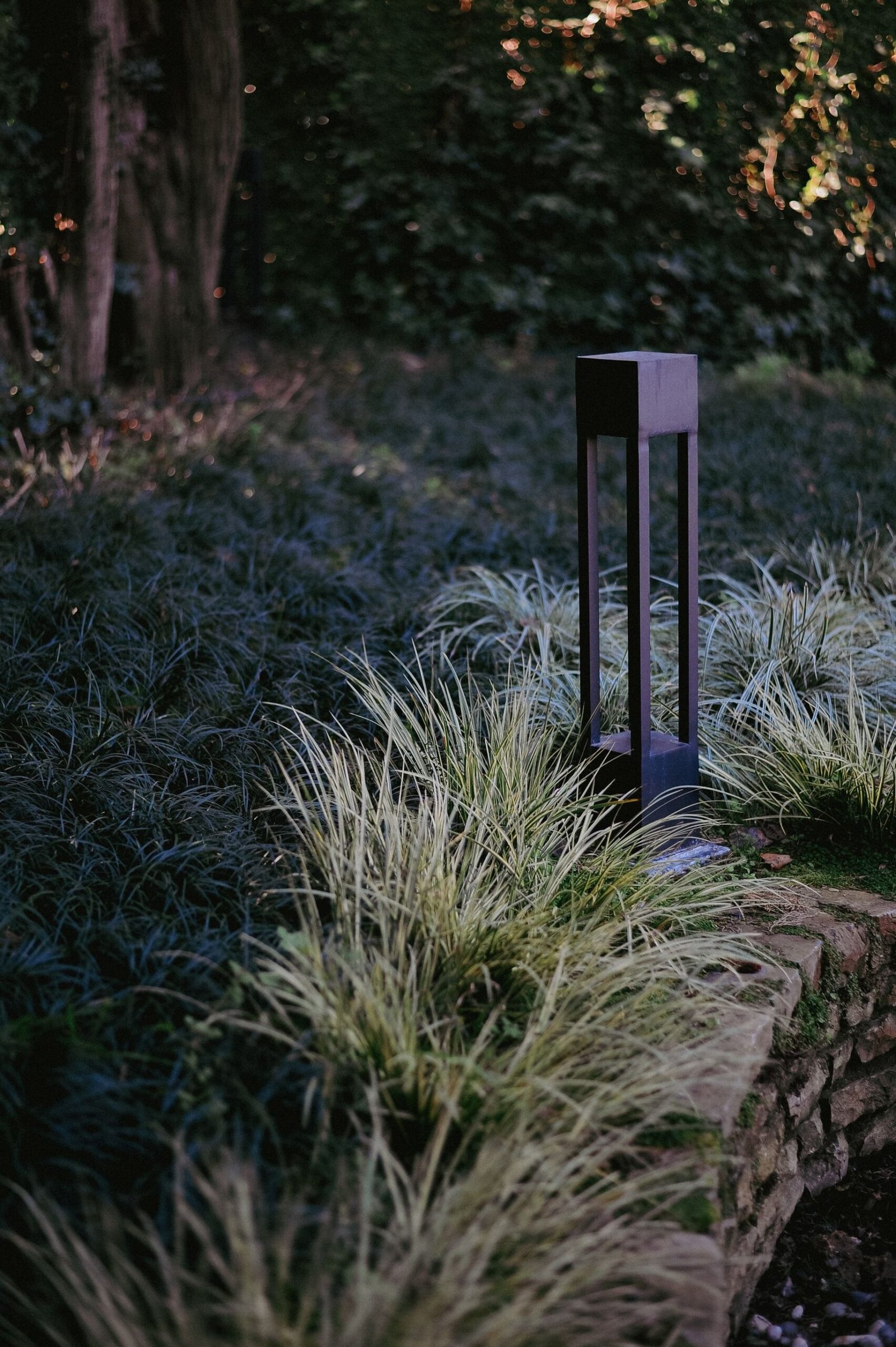 Tall modern black lantern standing in garden grass at night