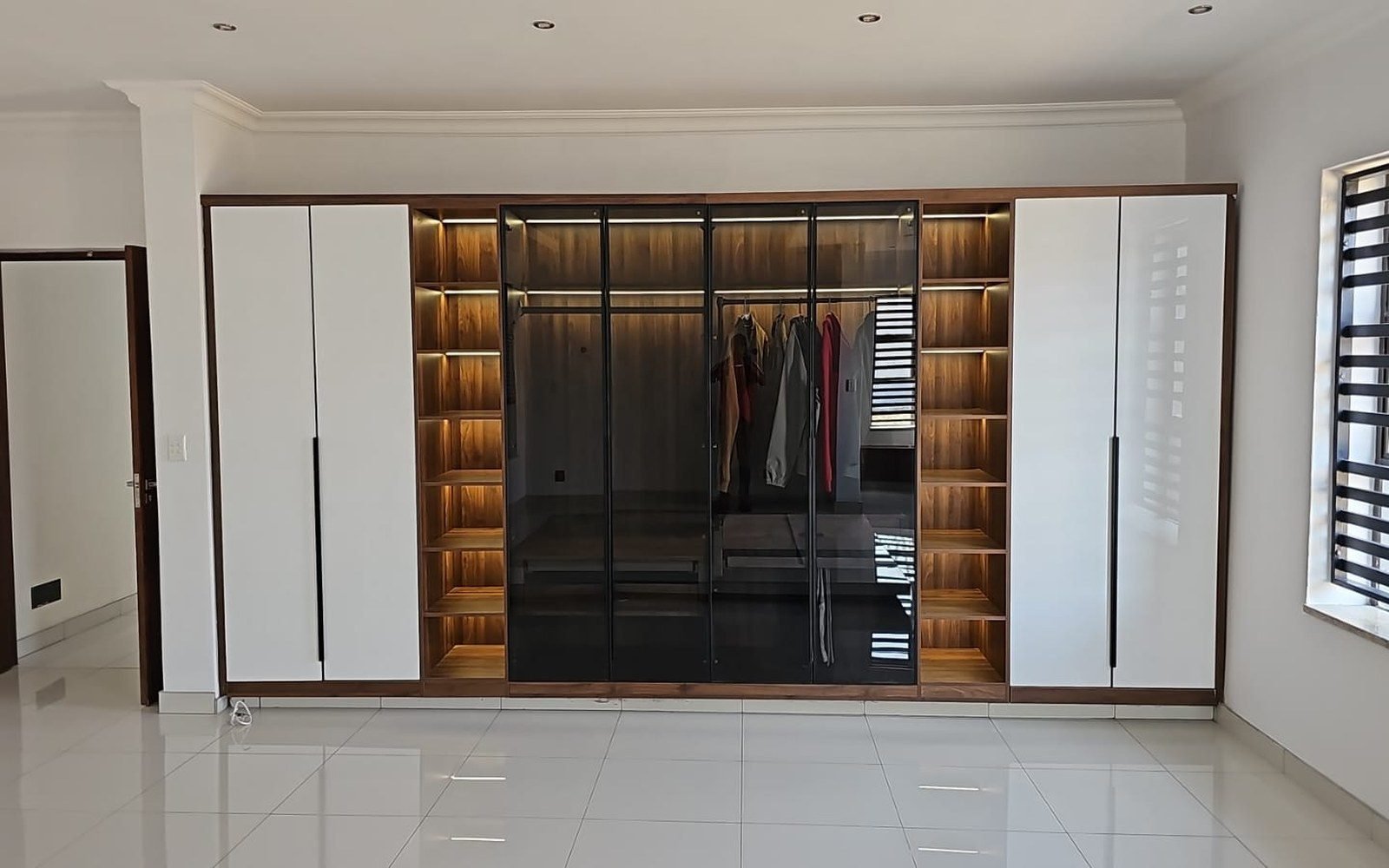 Installed villa wardrobe wall with white gloss doors, wood lined open hanging bays and mirror sliding doors