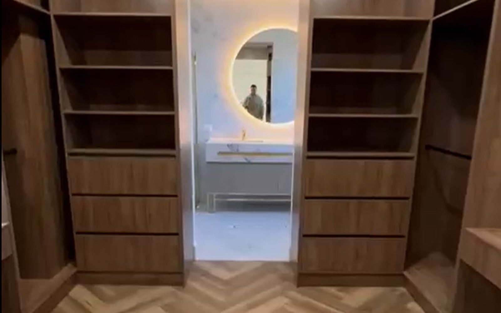 Open walnut walk-in closet with adjustable shelves, drawers and hanging rails seen through the room