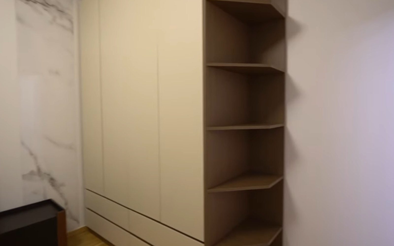 Full height white wardrobe with an open shelf column beside a marble effect wall in a villa bedroom