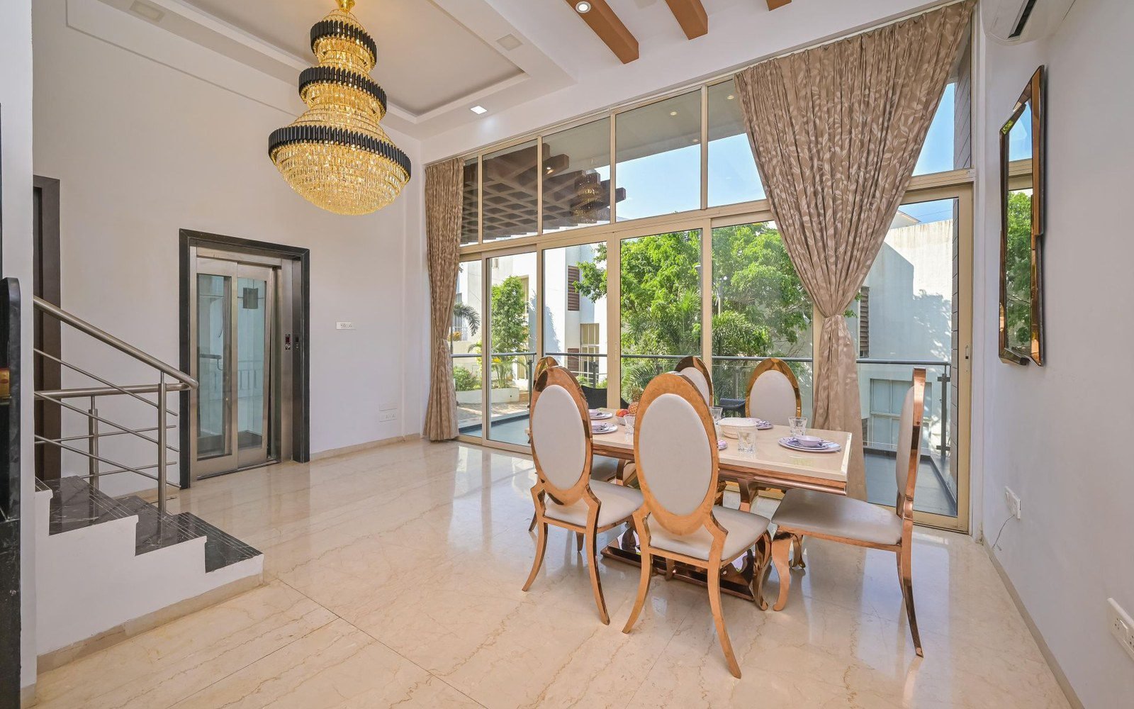 Floor-to-ceiling sliding glass wall in a double-height villa dining room
