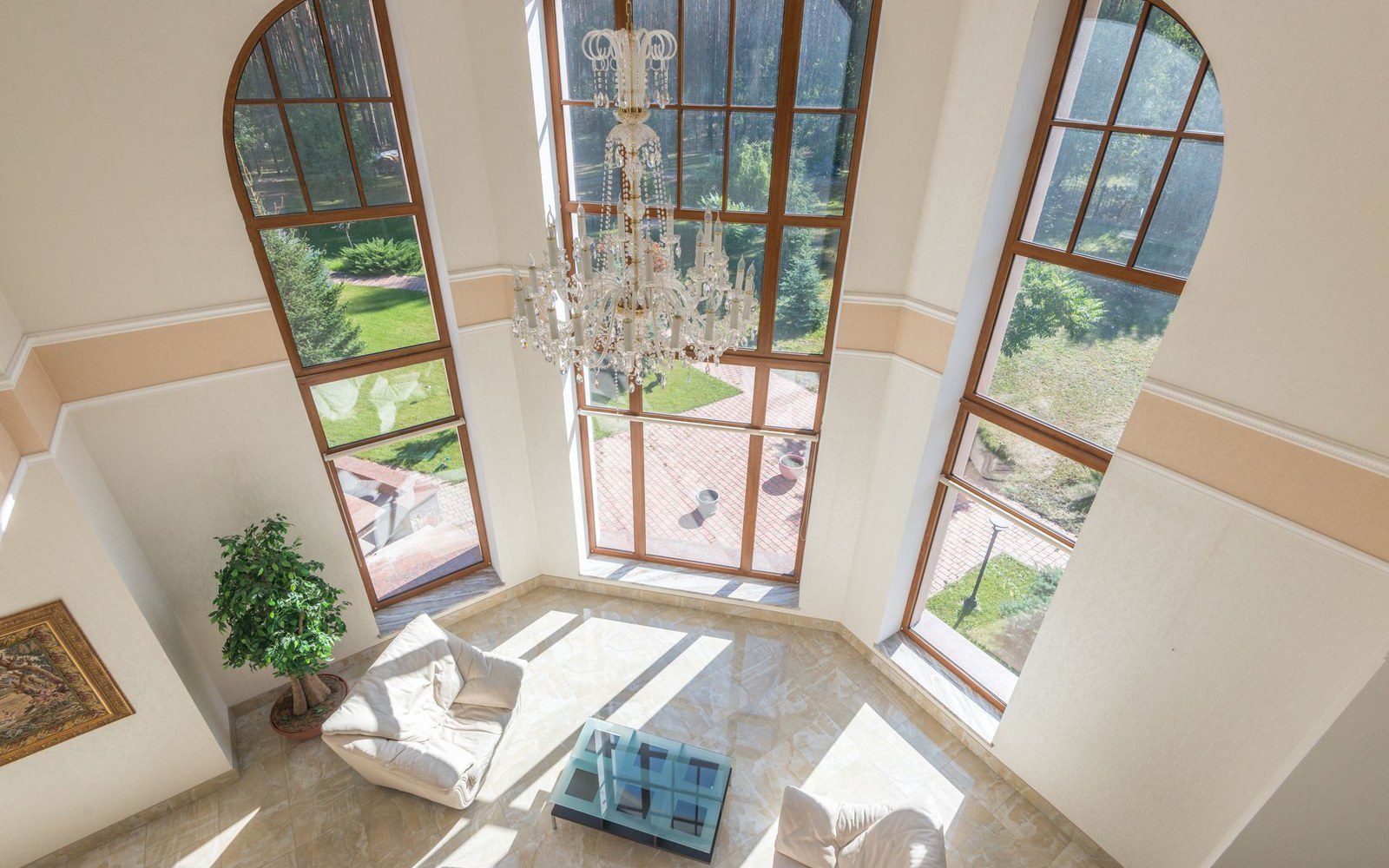 Tall arched windows in a double-height villa atrium with a chandelier