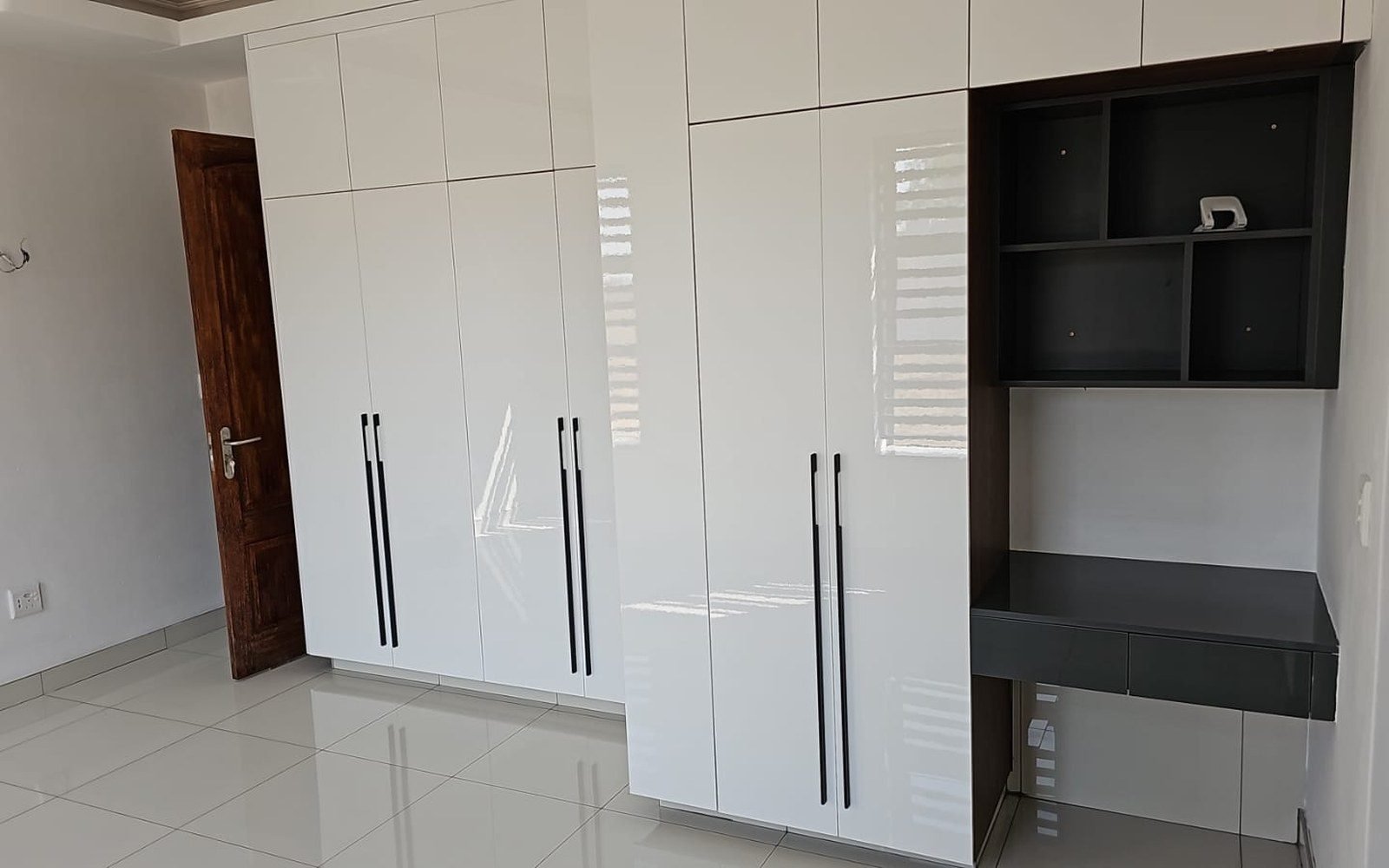 Full-height white high-gloss built-in wardrobe with desk, floor to ceiling, in a villa bedroom